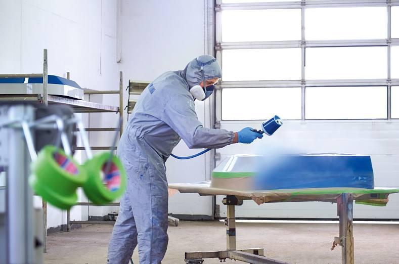 a worker spray-painting a surface while tesa 4338 high performance masking tape protects the rest of the surface.